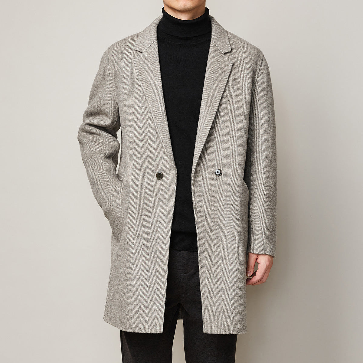 Man wearing a light grey wool overcoat in herringbone pattern with notch lapel layered over a black
turtleneck.