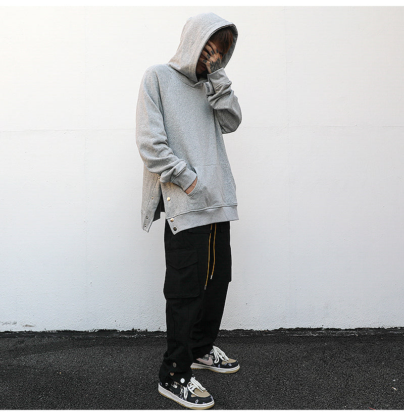 Man wearing a minimalist oversized black hoodie with a front pocket and side snap-button details.