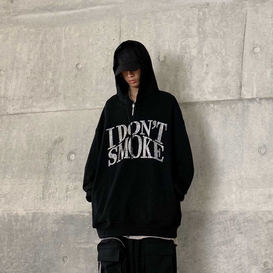 Man wearing an oversized black hoodie with a sparkling rhinestone “I Don’t Smoke” graphic on the front, 
styled with black cargo pants and a cap.