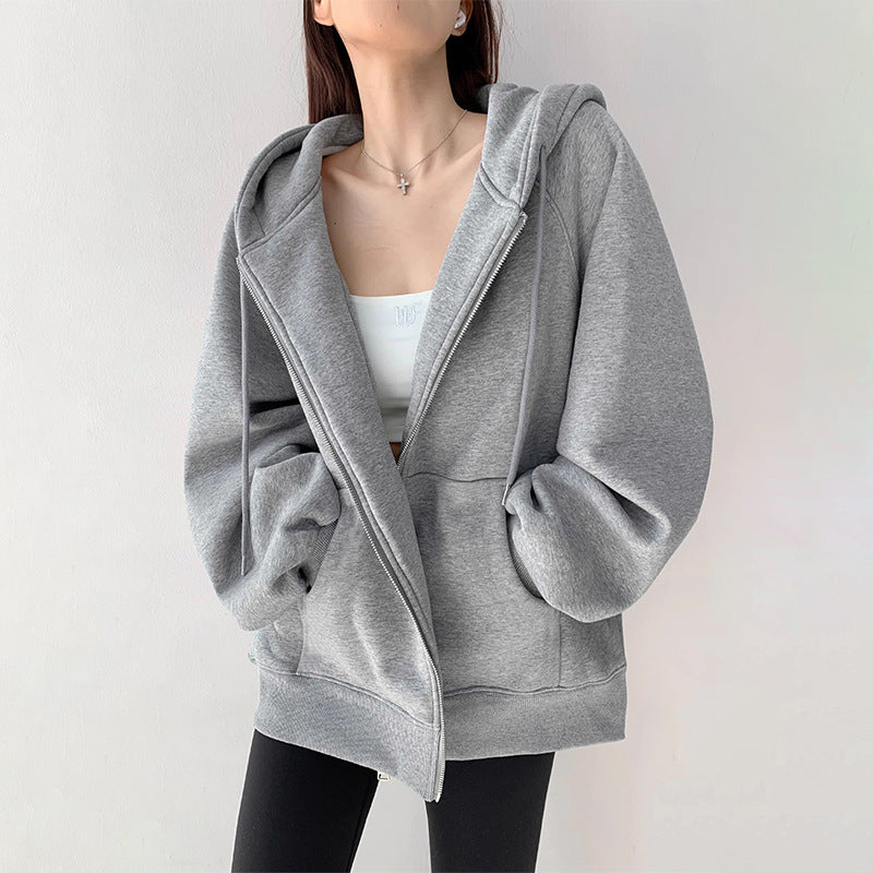 Woman wearing a grey oversized zip-up hoodie sweatshirt with hood and front zipper, styled with white crop 
top and black leggings. 