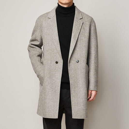 Man wearing a light grey wool overcoat in herringbone pattern with notch lapel layered over a black 
turtleneck. 