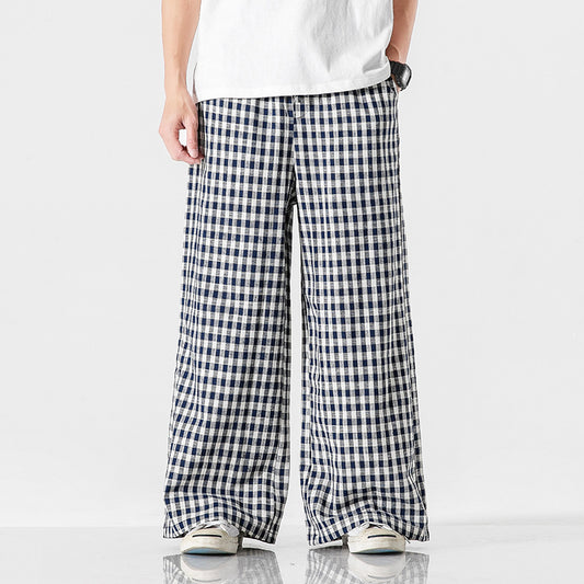 Man wearing black and white plaid wide leg cotton pants paired with sneakers against a light background.