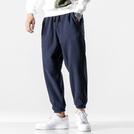Man wearing gray fleece jogger sweatpants with drawstring waist and cuffed ankles styled with white 
sneakers. 