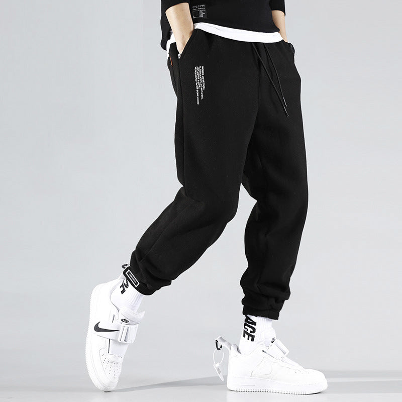 Man wearing black jogger sweatpants with cuffed ankles and graphic detail styled with white sneakers.
