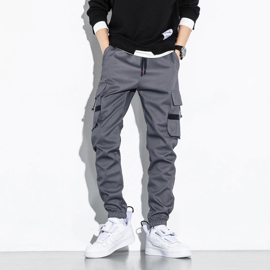 Men’s grey cargo jogger pants with multiple utility pockets and elastic ankle cuffs worn with white sneakers.