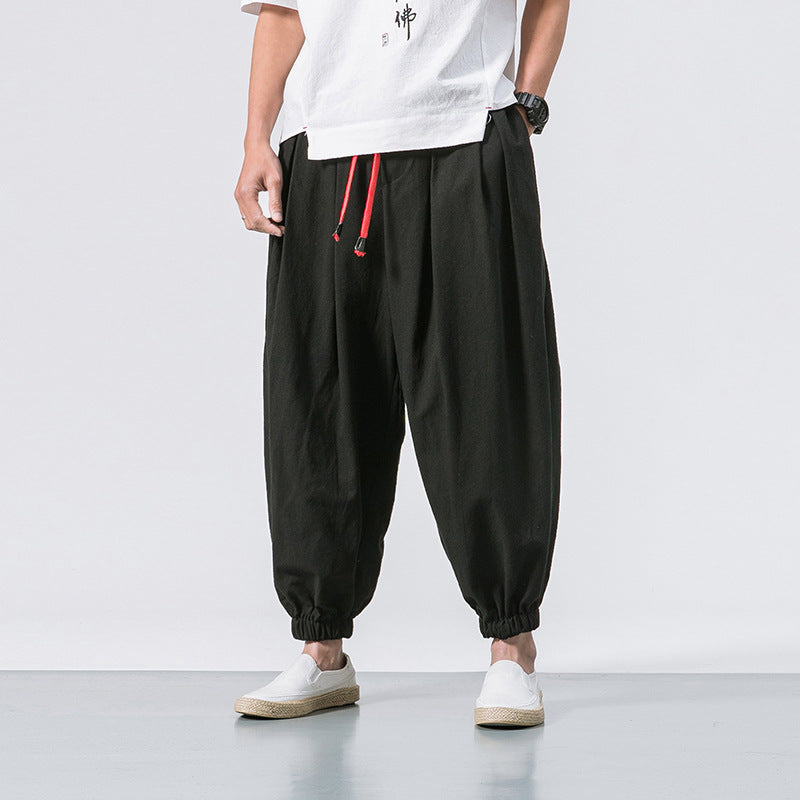 Men’s olive green linen harem pants with elastic ankle cuffs and drawstring waistband worn with slip-on 
shoes. 