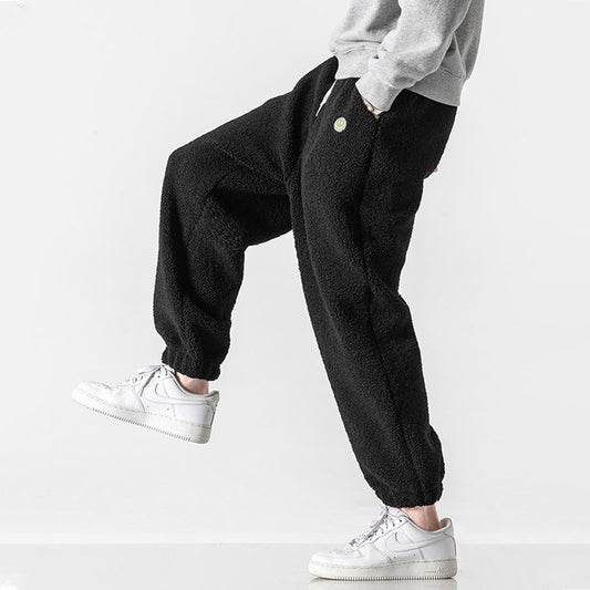 Man wearing olive green fleece jogger pants with plush texture and cuffed ankles paired with sneakers. 