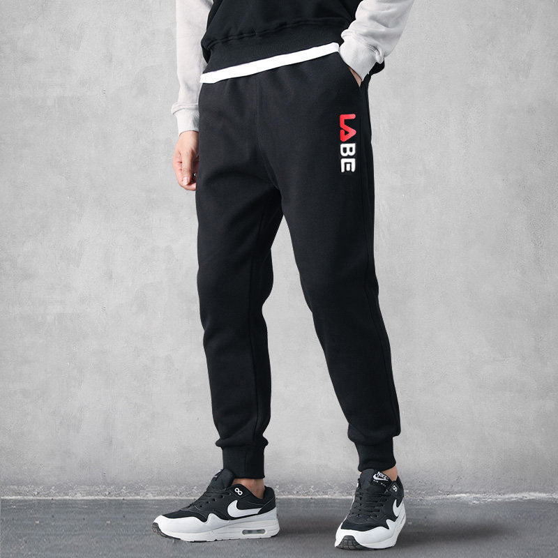 Man wearing black tapered jogger sweatpants with vertical logo print and cuffed ankles paired with 
sneakers. 