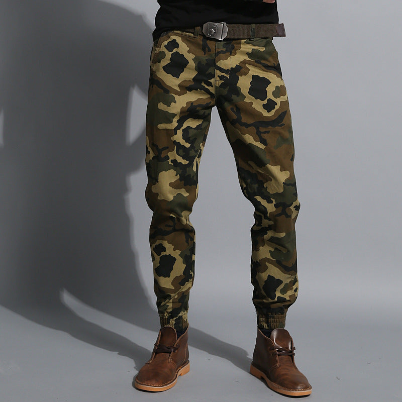 Men’s green camouflage slim fit tactical pants worn with tan boots against a dark textured background. 