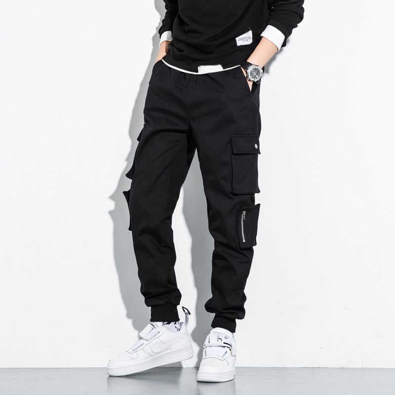 Men’s grey slim fit cargo pants with multiple utility pockets and drawstring worn with white sneakers against 
a white background. 