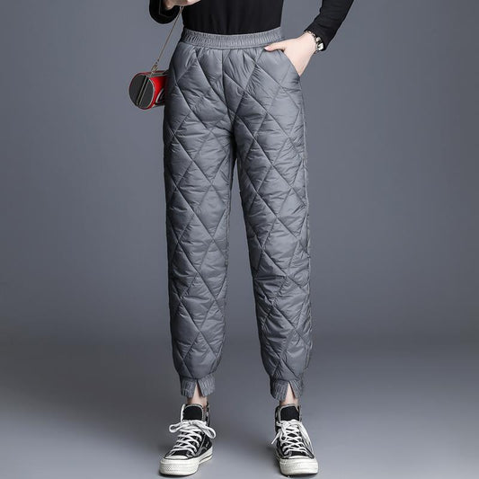 Woman wearing high-waisted black quilted puffer pants with elastic waistband and cuffed ankles styled with 
sneakers. 