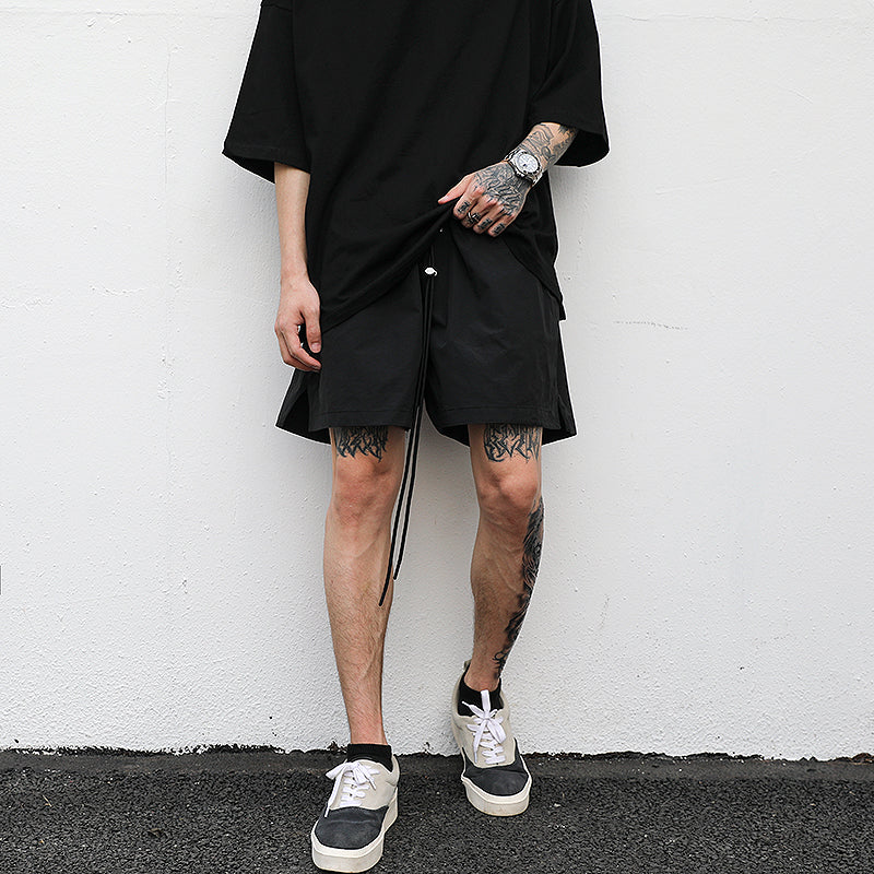 Man wearing relaxed fit minimal black drawstring streetwear shorts with oversized black t-shirt and 
skate-style sneakers. 