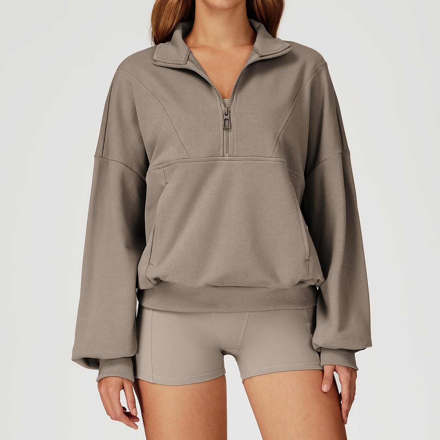 Woman wearing a beige oversized half-zip sweatshirt with high collar, styled with matching biker shorts. 