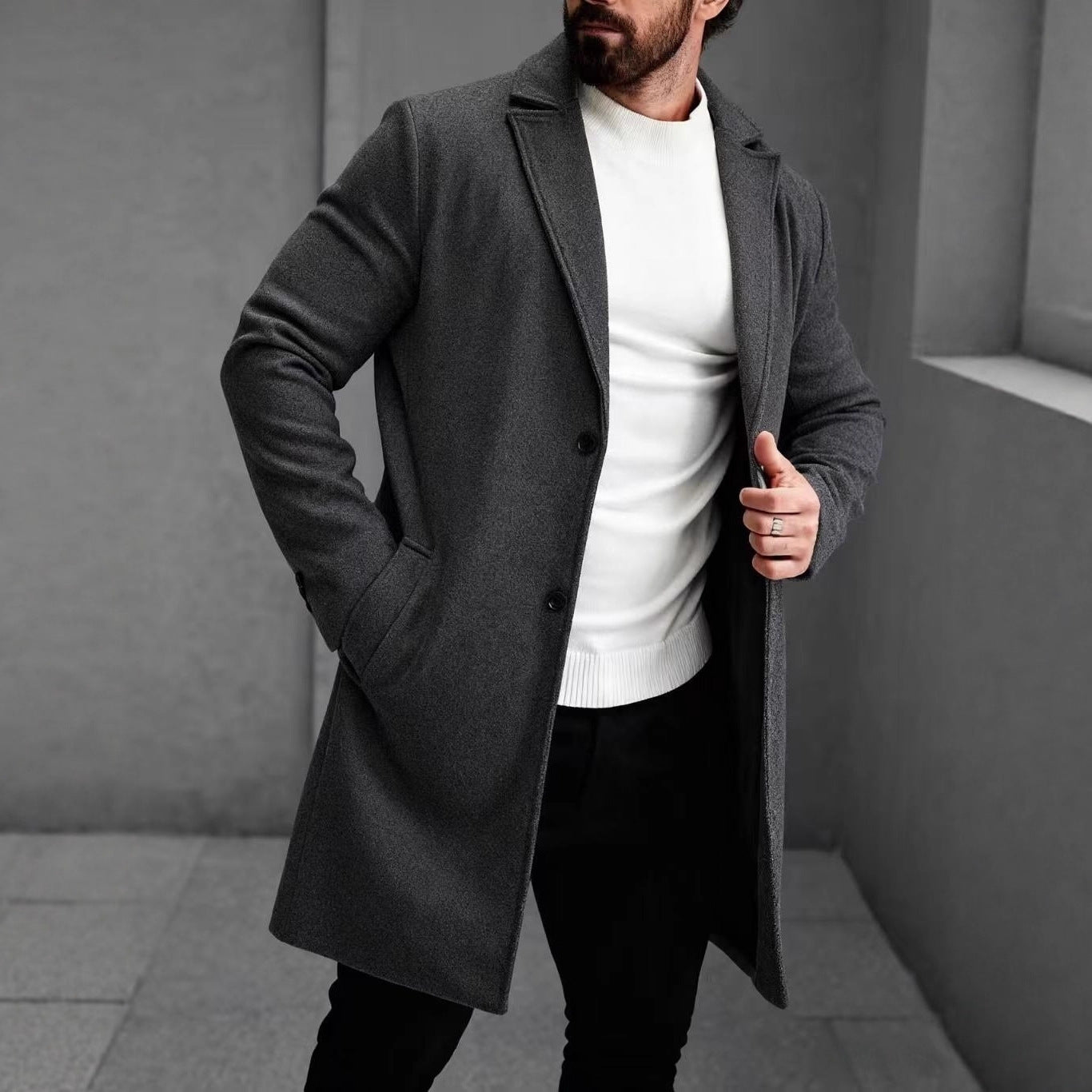 Man wearing a black tailored overcoat with notch lapel over a white sweater and black trousers