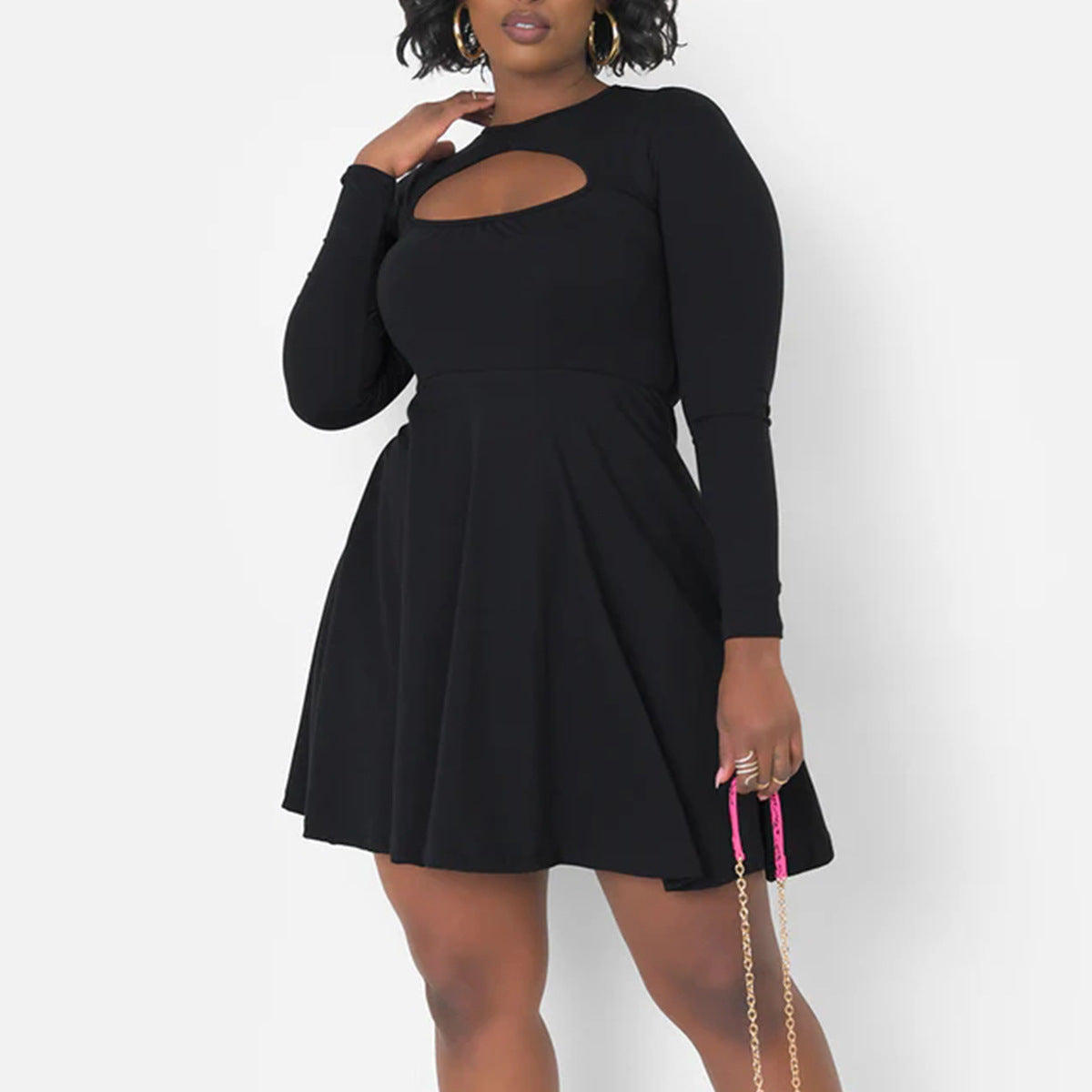 Plus size model wearing a black long sleeve mini dress with cutout, styled with a pink mini bag and gold 
accessories. 