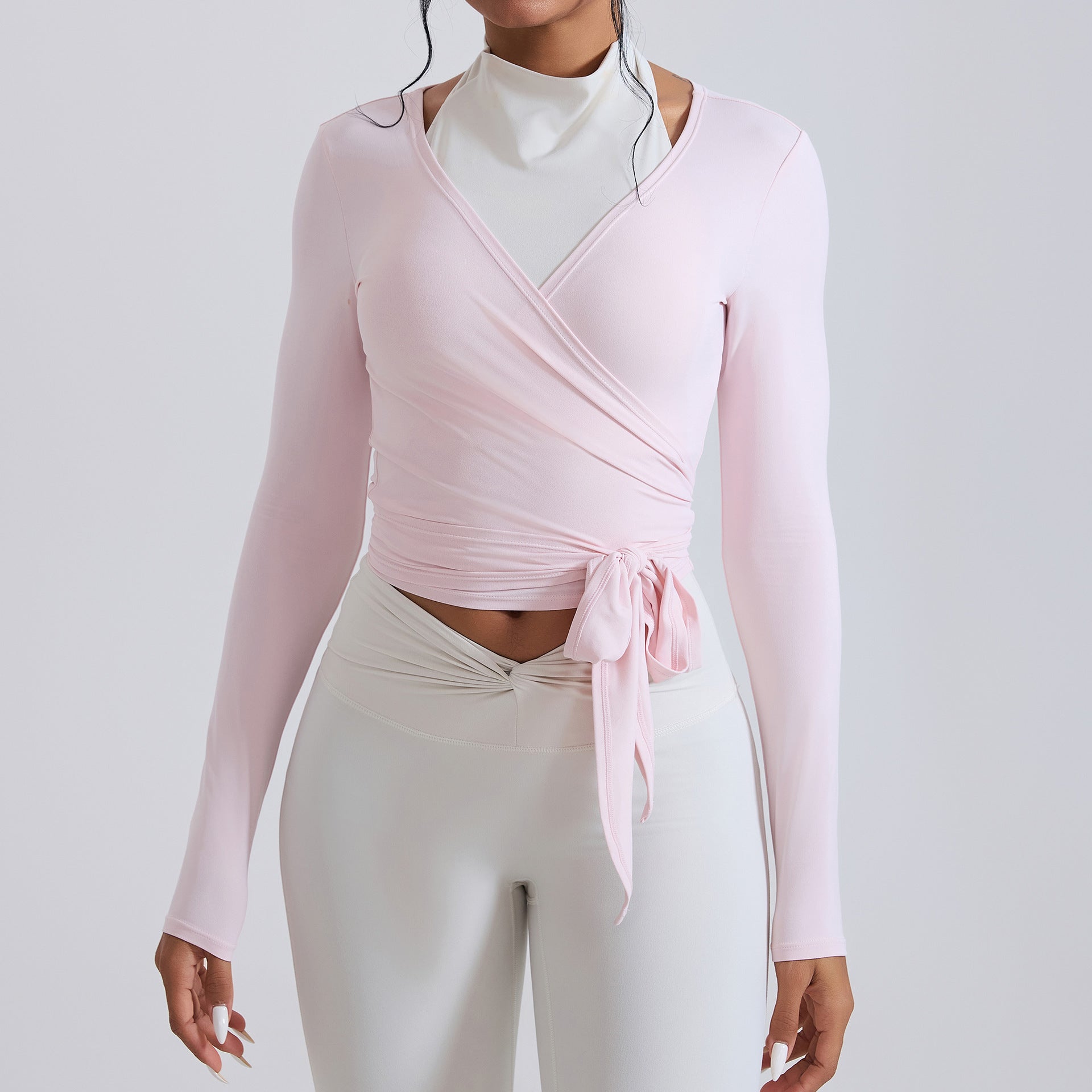 Woman wearing a black long sleeve wrap crop top with mock neck detail and adjustable tie waist.