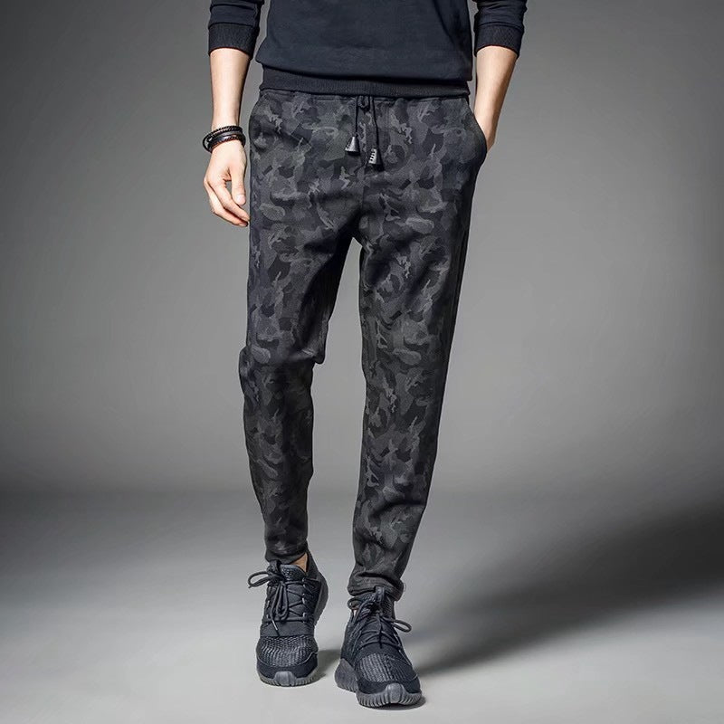 Man wearing dark camouflage slim-fit jogger pants with drawstring waist and black athletic sneakers. 