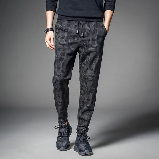 Man wearing dark camouflage slim-fit jogger pants with drawstring waist and black athletic sneakers. 