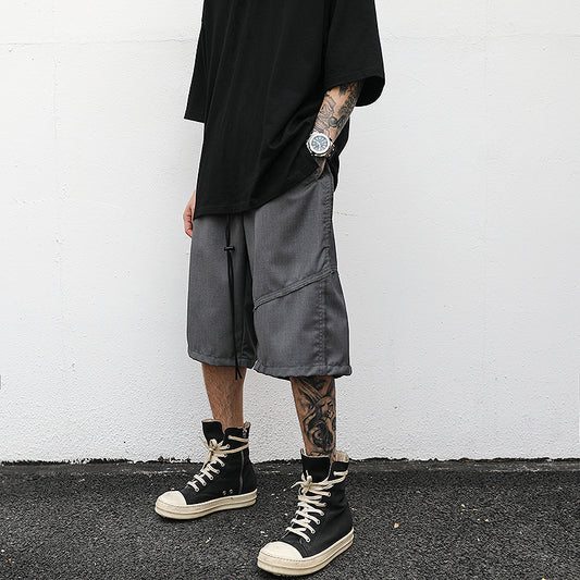 Man wearing longline black utility panel streetwear shorts with oversized black t-shirt and high-top sneakers.