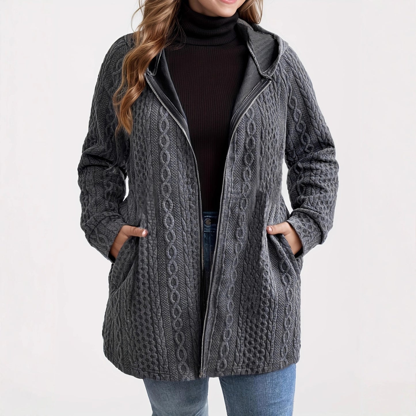 Woman wearing a charcoal grey cable knit hooded zip-up jacket with side pockets, styled with denim pants 
and black turtleneck top. 