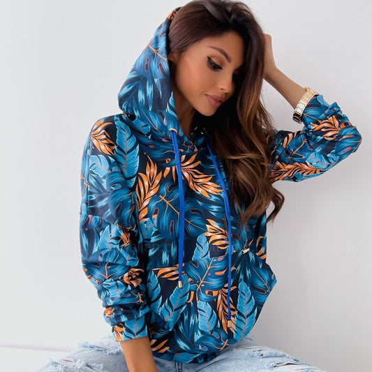 Woman wearing a blue tropical leaf print pullover hoodie with drawstring hood and front pouch pocket. 