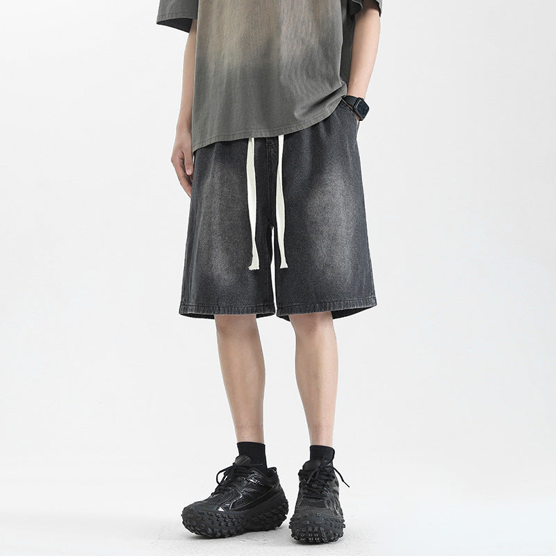 Man wearing washed dark grey denim-style drawstring streetwear shorts with black sneakers.