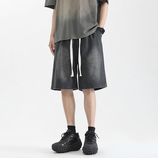 Man wearing washed dark grey denim-style drawstring streetwear shorts with black sneakers.