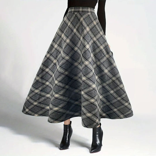 Woman wearing a high-waisted grey plaid A-line maxi skirt with flared hem and black ankle boots.