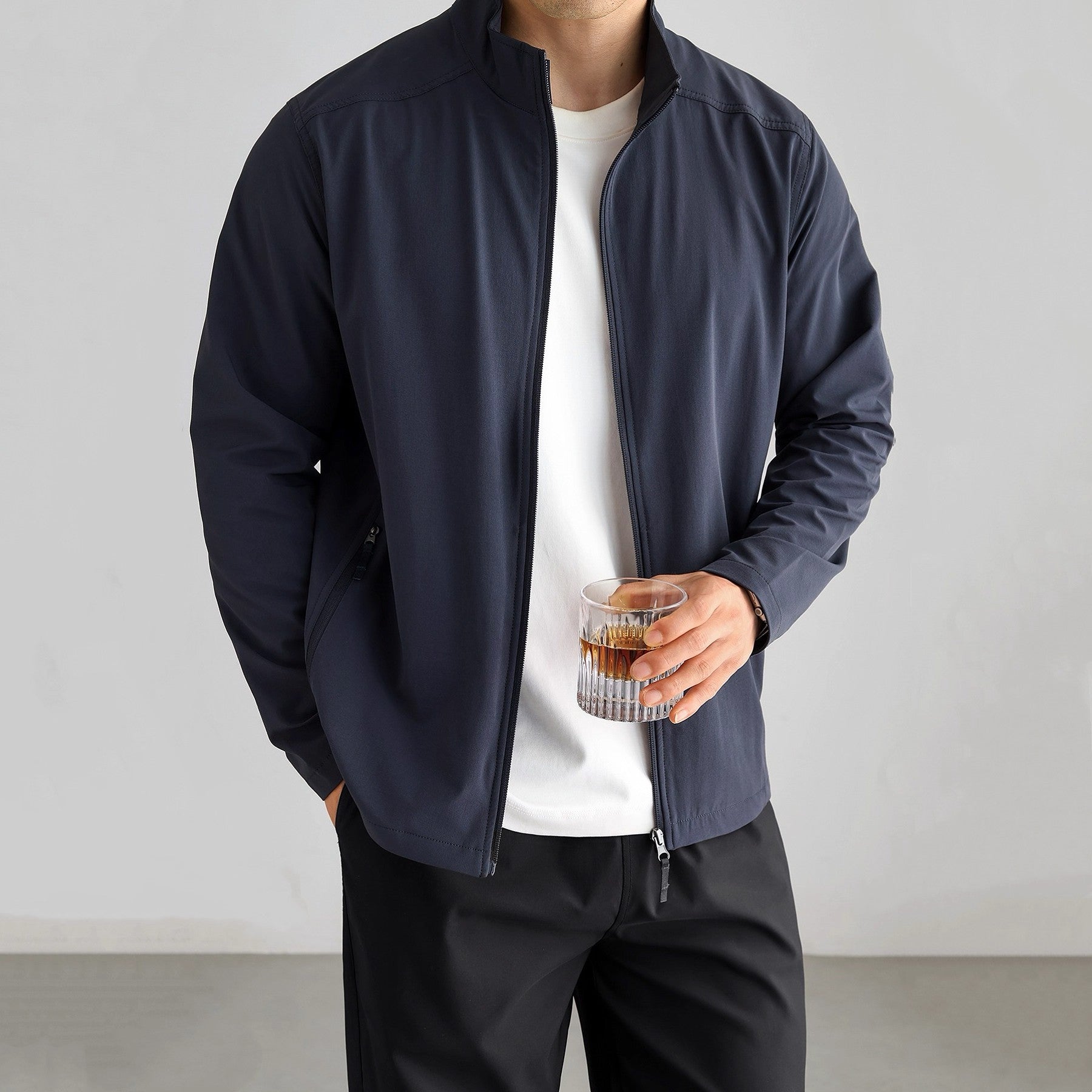 Man wearing a navy blue zip-up lightweight jacket with stand collar over a white t-shirt.
