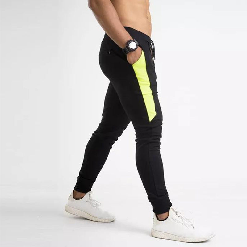 Man wearing black slim fit training joggers with neon contrast side panel and cuffed ankles paired with white 
sneakers. 
