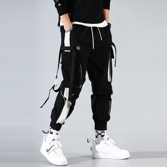 Man wearing black techwear cargo jogger pants with utility straps, multiple pockets, and cuffed ankles 
styled with white high-top sneakers.