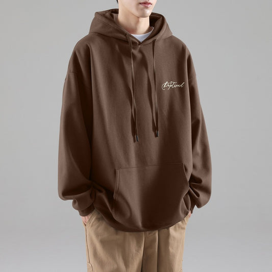 Man wearing a beige minimalist hoodie with a small script logo on the chest, front pouch pocket, and 
drawstring hood, styled with light blue jeans.