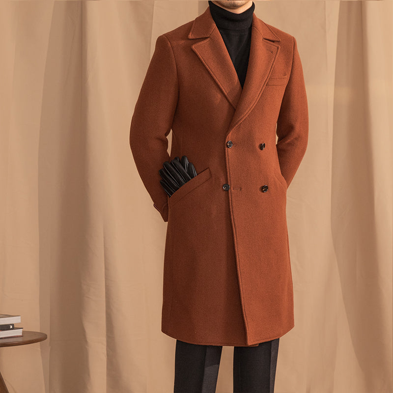 Man wearing a brown double-breasted wool overcoat with peak lapel over a black turtleneck and leather 
gloves in pocket. 