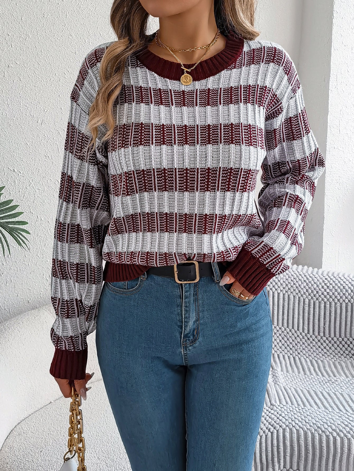Woman wearing a beige and black striped rib knit crewneck sweater, styled with blue jeans, belt, gold 
jewelry and a handbag. 