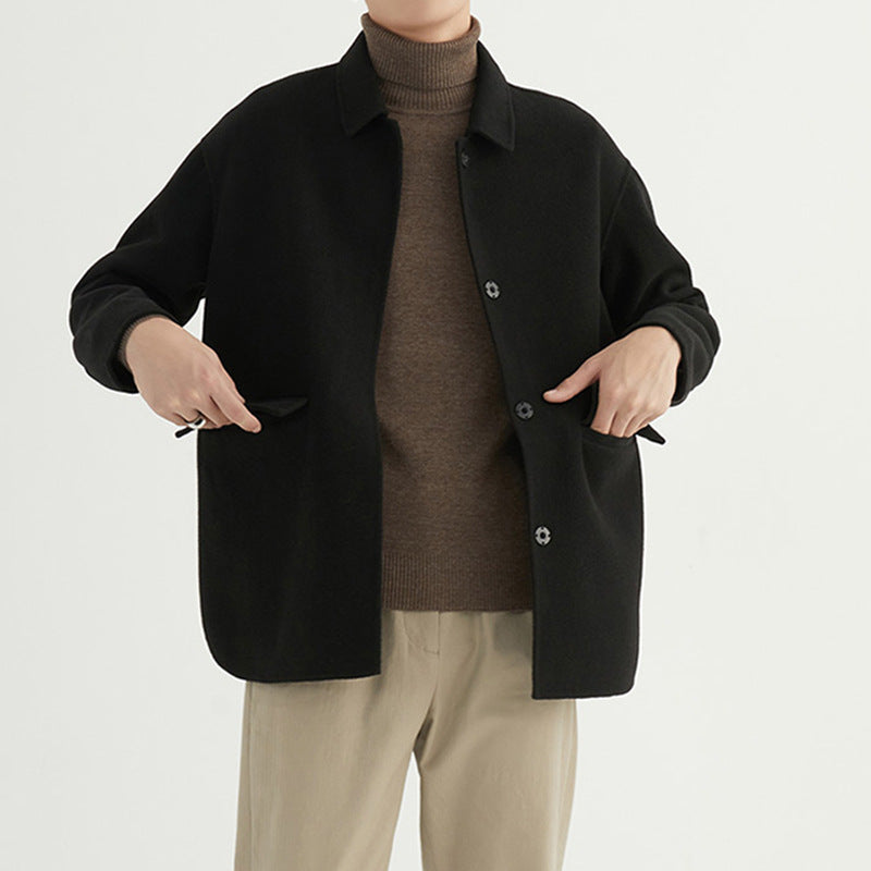 Man wearing a black wool button-up overcoat layered over a brown turtleneck sweater.