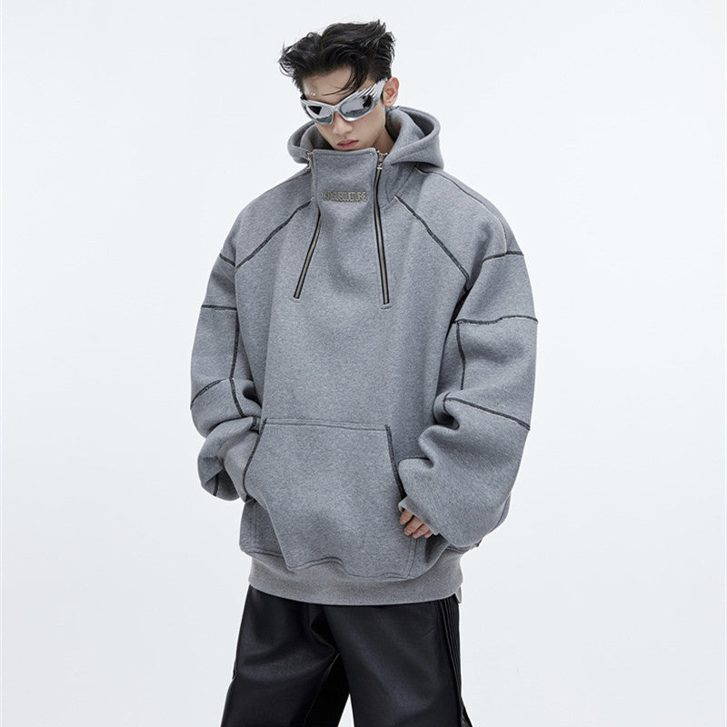 Man wearing an oversized black fleece techwear hoodie with contrast stitching, a structured hood, and a 
front pocket, styled with wide-leg black pants.