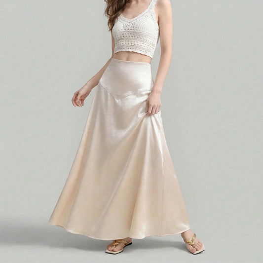 Woman wearing a high-waisted cream satin maxi skirt with flowy A-line silhouette, styled with a crochet crop 
top. 