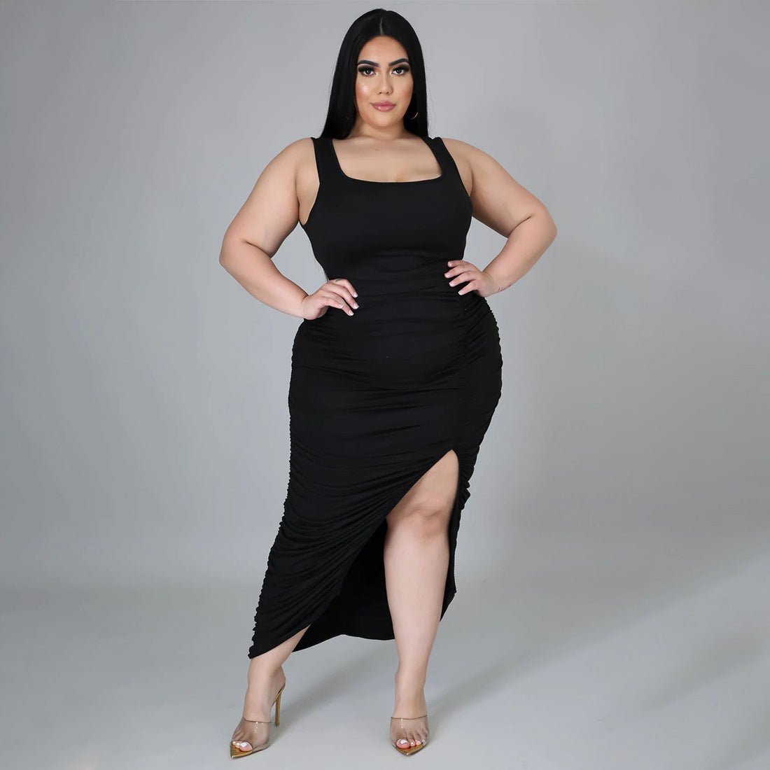 Plus size woman wearing a black ruched bodycon midi dress with square neckline and front slit. 
