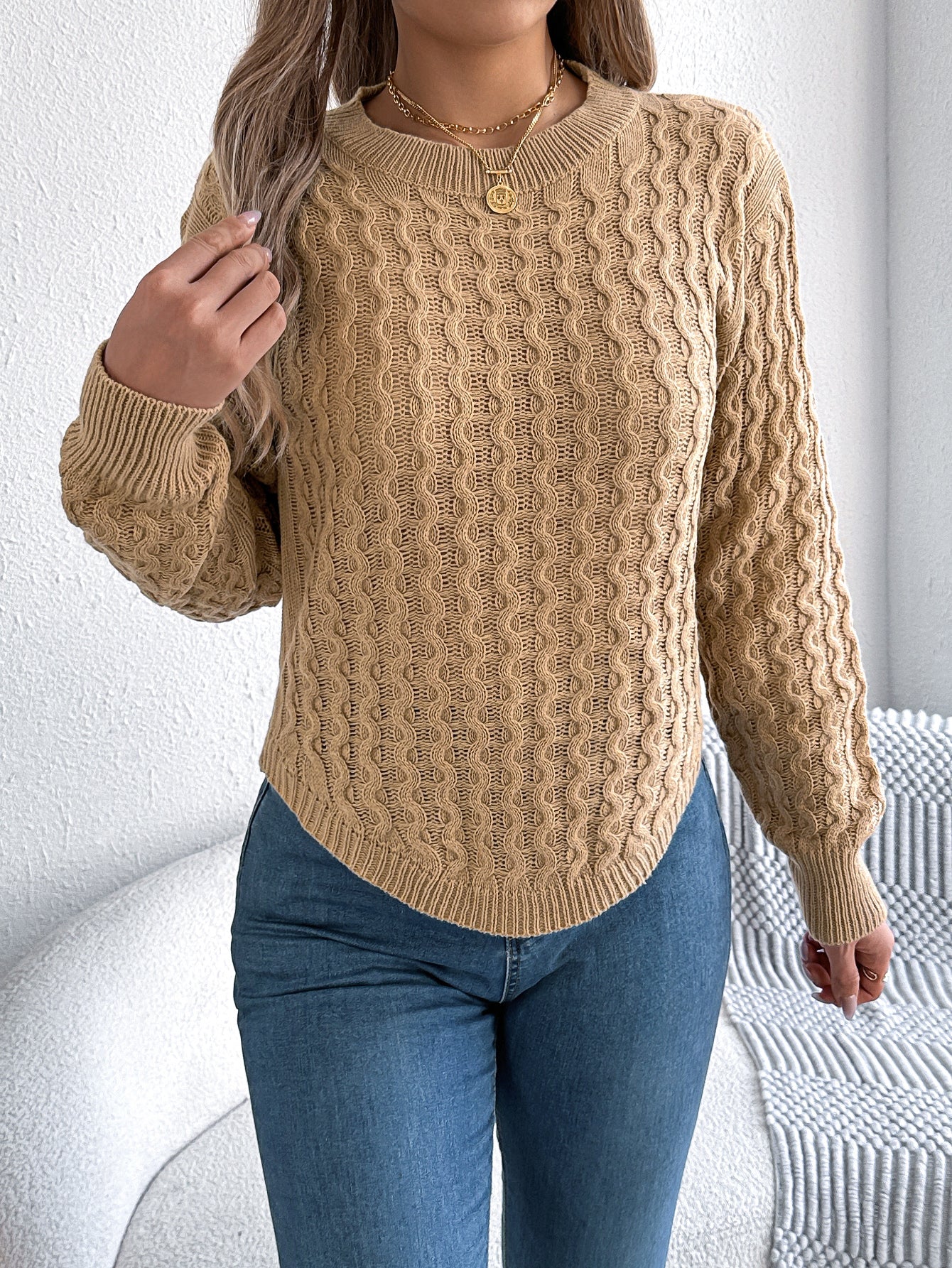 Woman wearing a burgundy cable knit crewneck sweater with textured pattern, styled with blue jeans and 
gold jewelry. 