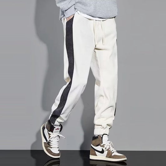 Man wearing gray jogger sweatpants with white side stripe, drawstring waist, and cuffed ankles styled with 
white sneakers.