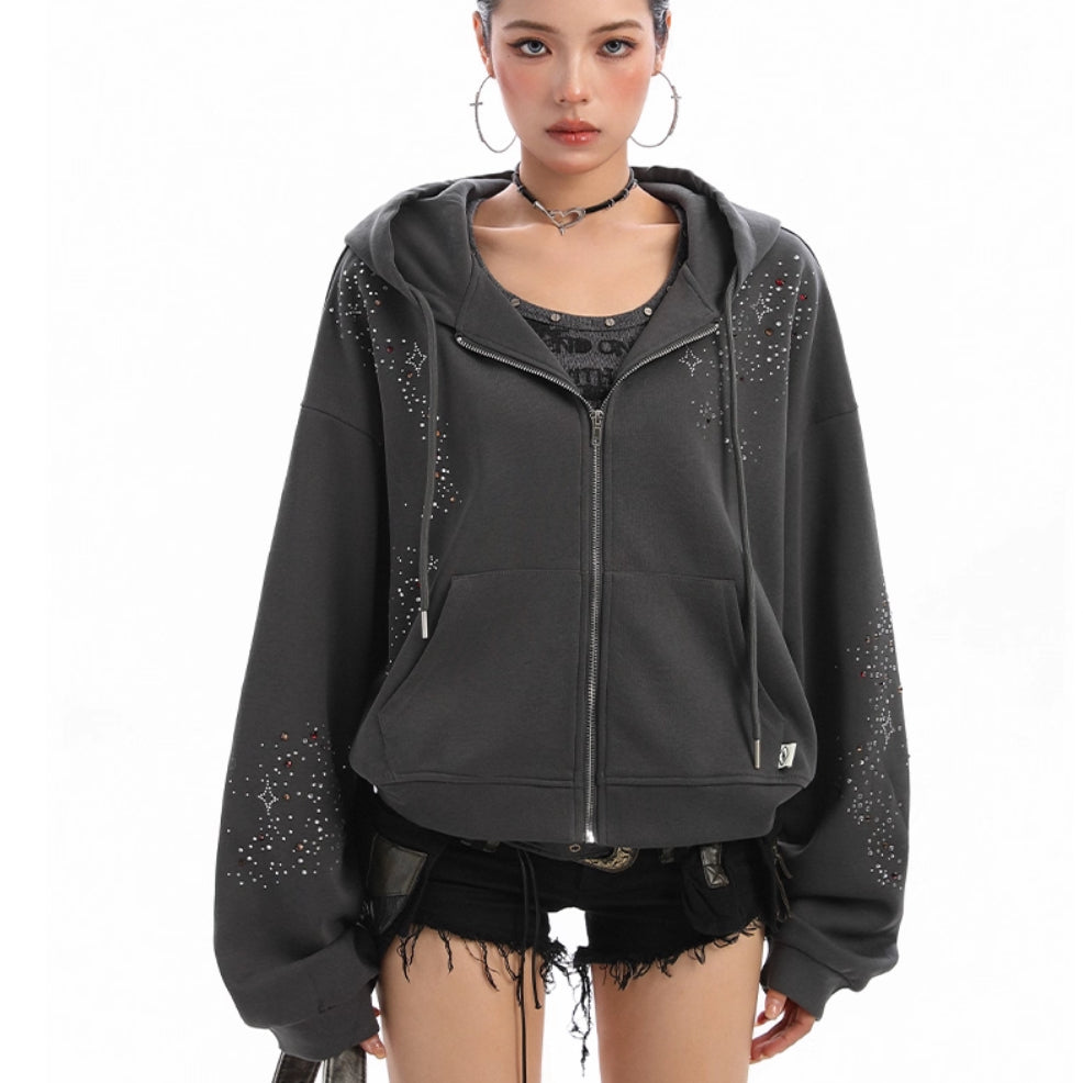 Woman wearing a dark grey oversized zip-up hoodie with rhinestone details on sleeves and chest, styled 
with shorts on a white background.