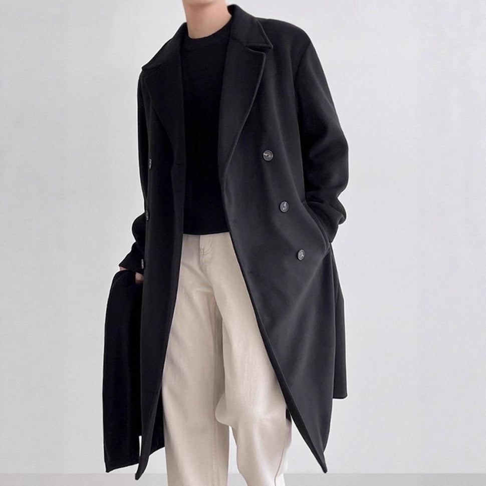 Man wearing a black double-breasted long overcoat layered over black top and light cream colored trousers.
