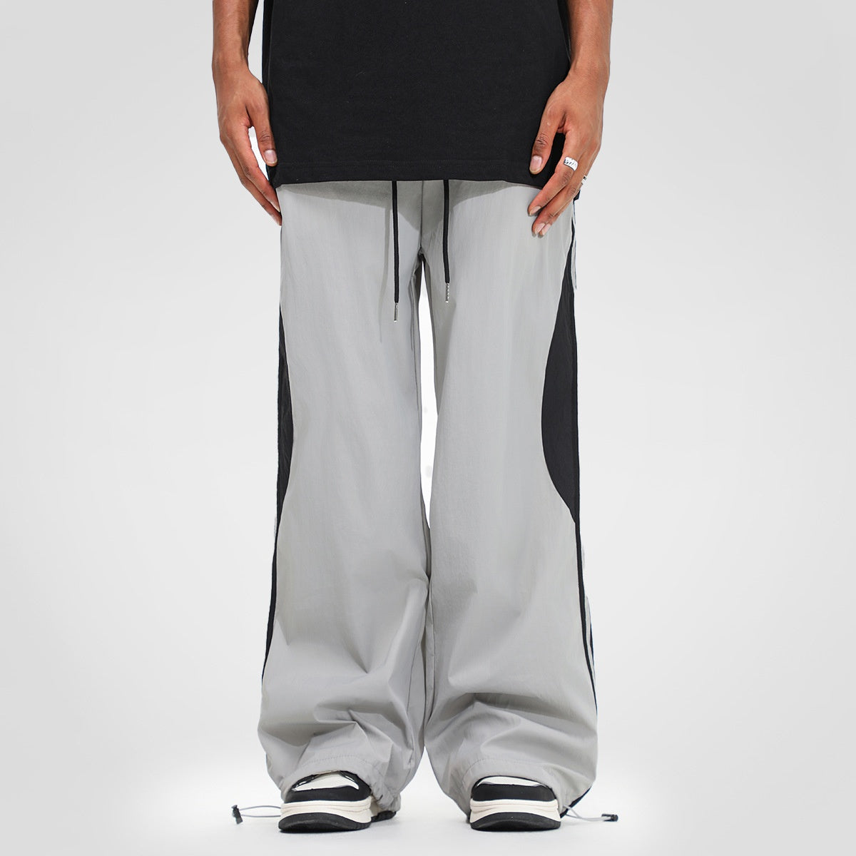 Men’s black nylon wide-leg track pants with elastic waistband, drawstring, grey contrast side panels, 
contrast lines on the sides and adjustable hem toggles.
