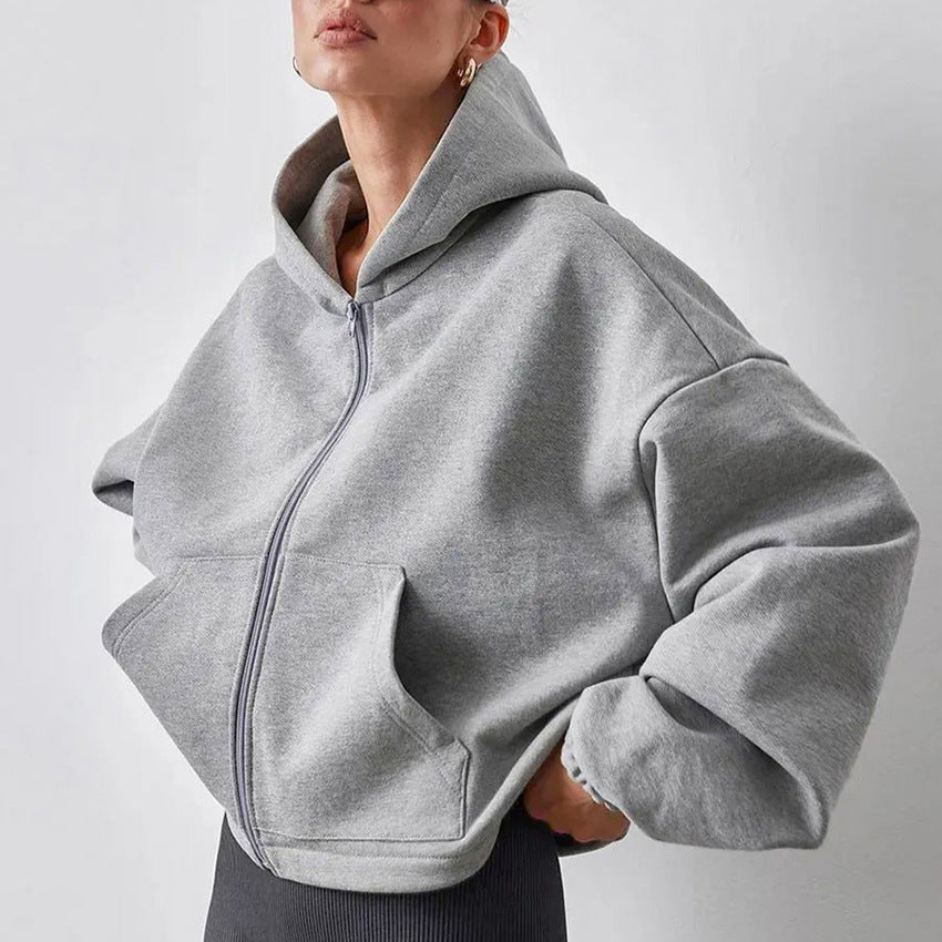 Woman wearing an oversized grey zip-up hoodie with hood, styled with grey leggings and gold earrings. 