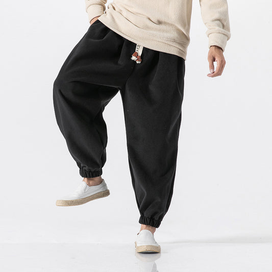 Men’s black relaxed fit jogger sweatpants with elastic waistband and ankle cuffs worn with light sneakers 
against a white background.