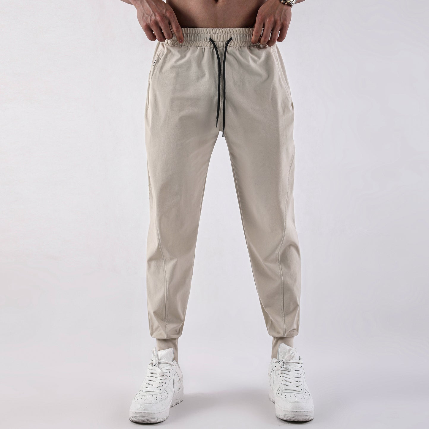 Man wearing beige lightweight jogger pants with elastic waistband and drawstring paired with white 
sneakers. 
