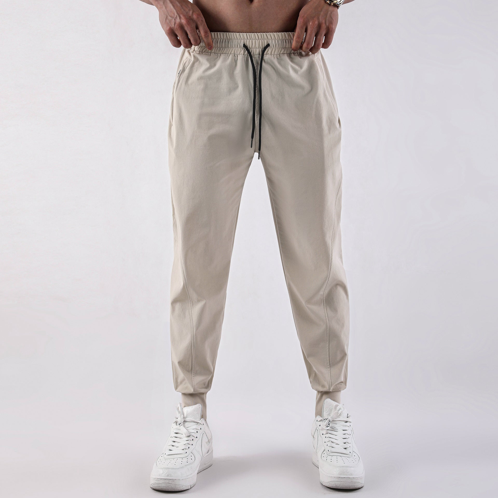 Man wearing beige lightweight jogger pants with elastic waistband and drawstring paired with white 
sneakers. 