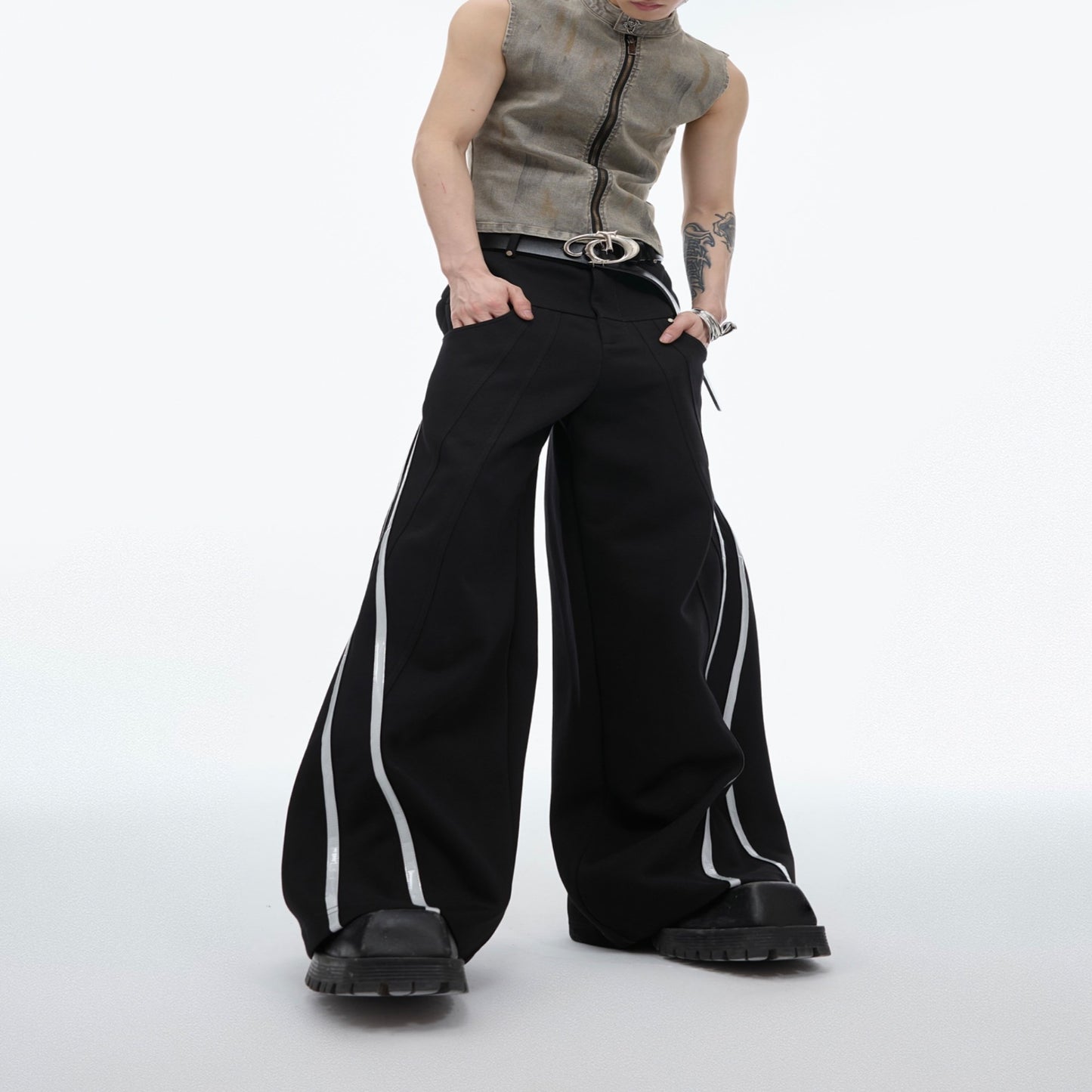 Men’s black wide-leg track pants with reflective side stripes worn with a matching jacket and chunky shoes.