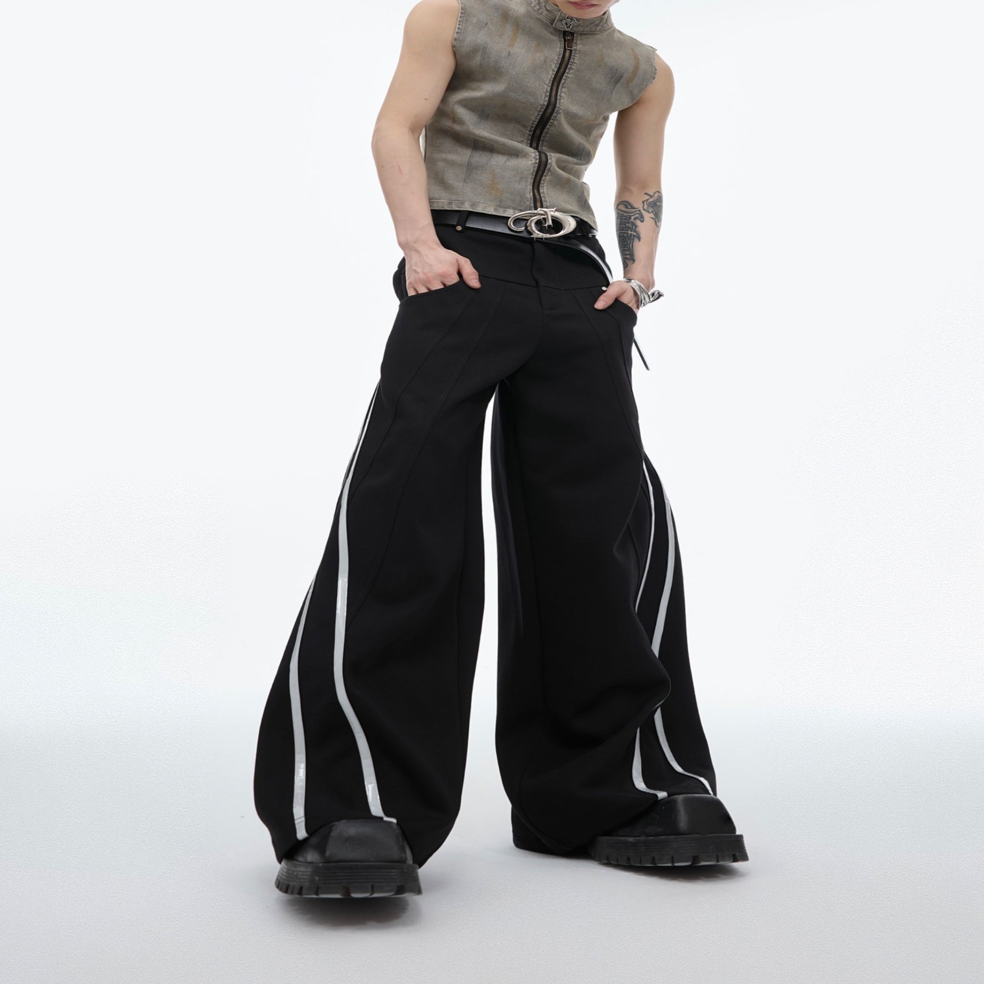 Men’s black wide-leg track pants with reflective side stripes worn with a matching jacket and chunky shoes.