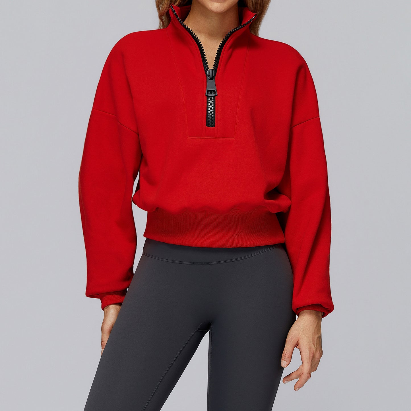 Woman wearing a black half-zip cropped oversized sweatshirt with high collar, styled with high-waisted 
leggings. 
